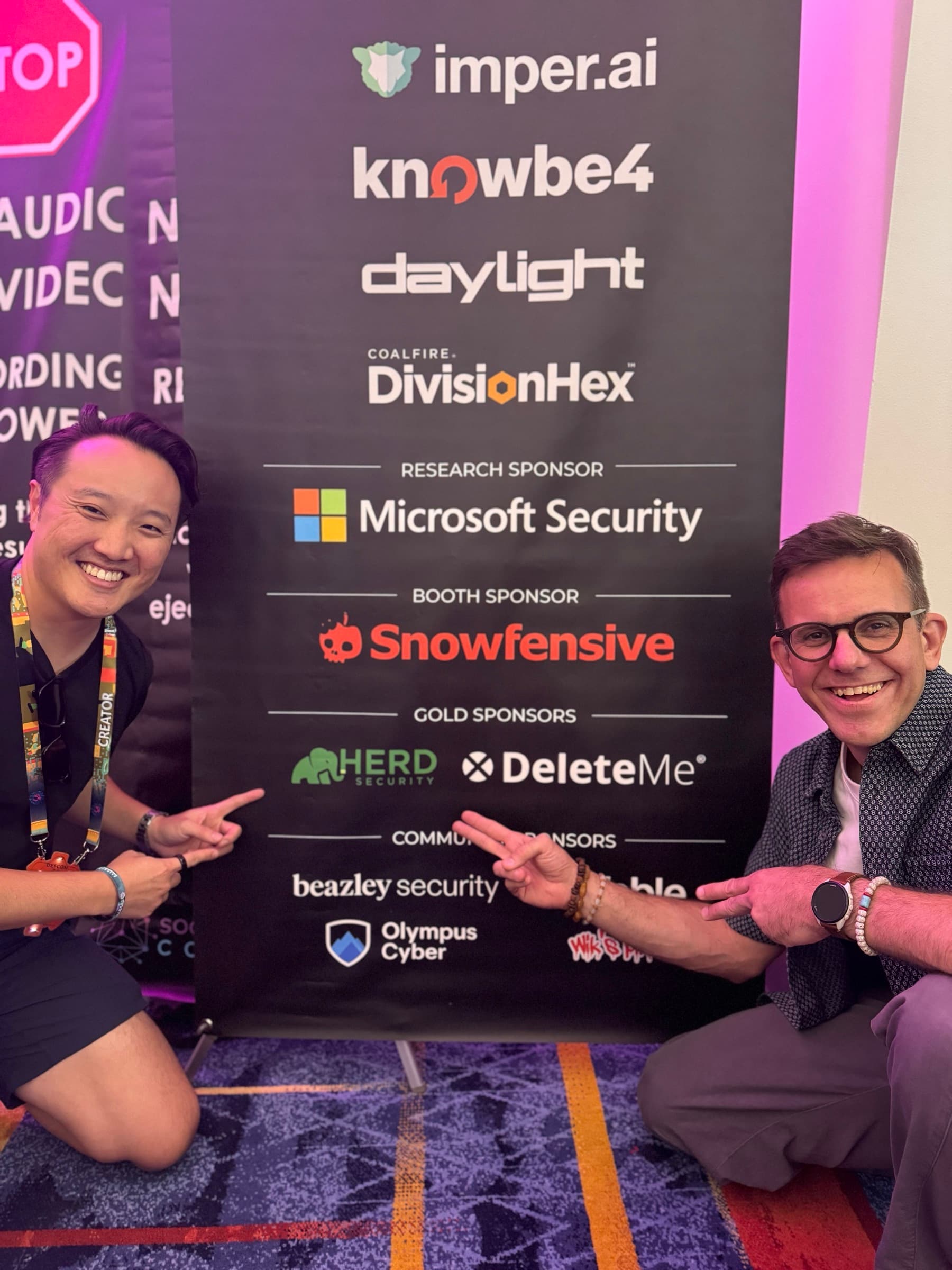 Herd Security team pointing at the Herd logo on the DEF CON sponsor banner